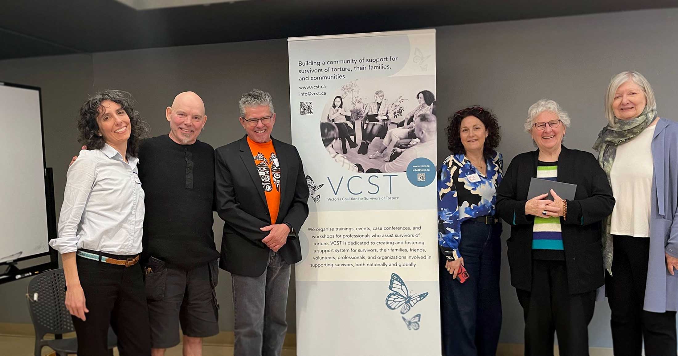 Melinda, Ken, Álvero and others stand by the VCST banner.